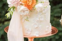 a sophisticated white buttercream wedding cake with sugar bloom patterns, white, blush and orange and ywllow blooms plus a white ribbon