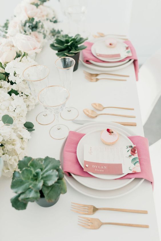 a stylish modern Valentine's Day wedding table with a blush and white floral runner, succulents, pink napkins and gold cutlery