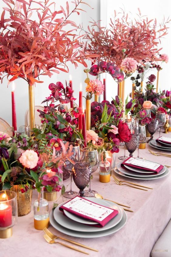 a super colorful Valentine's Day wedding table with a pink tablecloth, grey plates, berry-hued napkins, bold blooms and candles