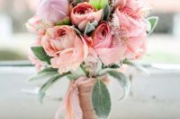 a sweet pastel Valentine wedding bouquet pf peachy and light pink blooms and greenery and light pink ribbons