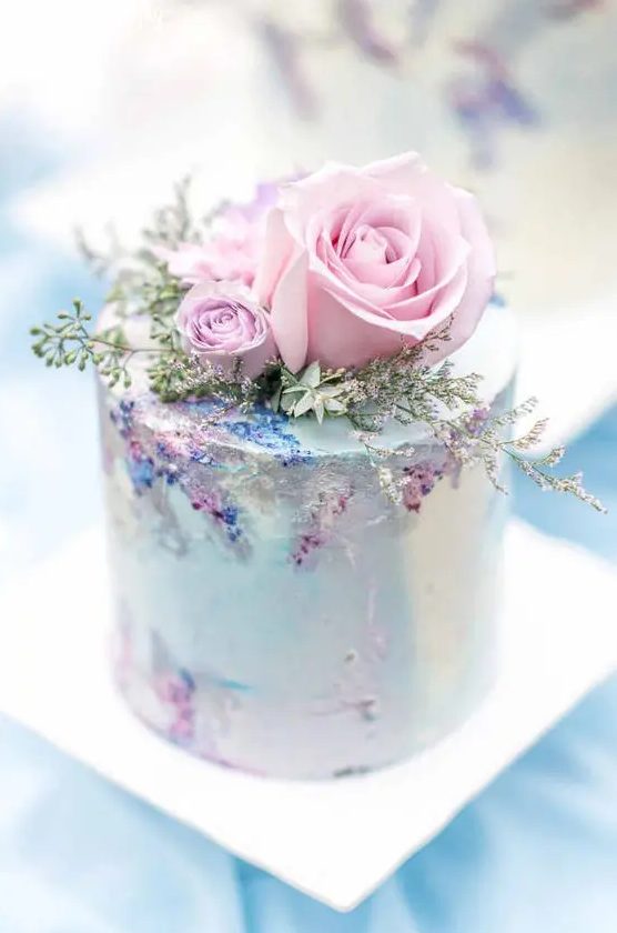 a very delicate and refined pastel wedding cake in light blue, with pink roses and greenery and sugar detailing is amazing for a secret garden wedding