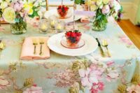a vintage pastel wedding tablescape with a chic floral tablecloth, pink napkins, pastel blooms and gold cutlery
