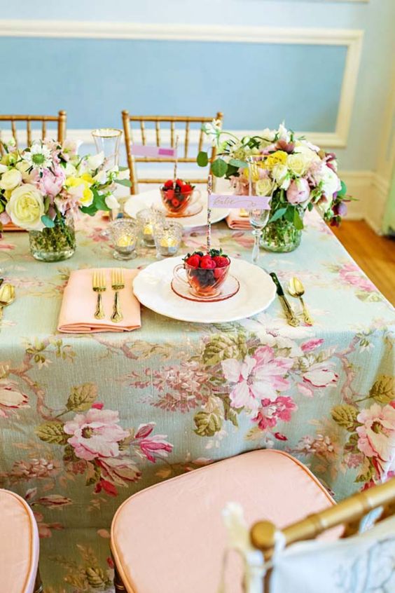 a vintage pastel wedding tablescape with a chic floral tablecloth, pink napkins, pastel blooms and gold cutlery