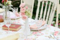 a vintage wedding tablescape with a bright floral tablecloth, pastel napkins, pastel blooms, vintage books and printed chargers