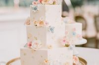 a white buttercream hexagon wedding cake with some painted and sugar blooms of pastel shades is beautiful