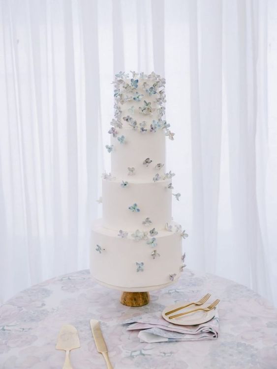 a white buttercream wedding cake topped with lilac and blue sugar blooms is a delicate and chic solution for a spring wedding