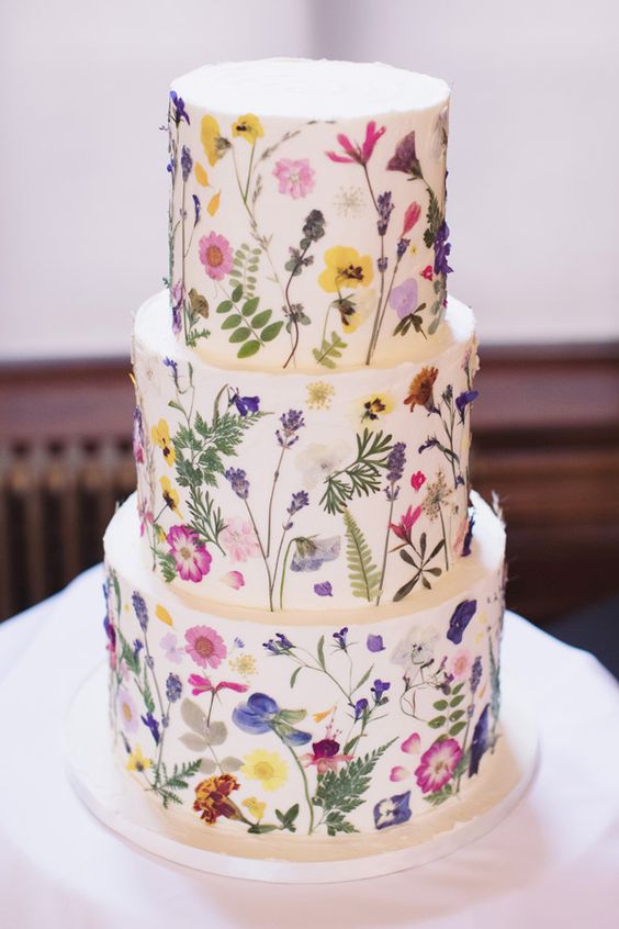 a white buttercream wedding cake with lots of pressed bright blooms is amazing for a spring or summer widlflower wedding