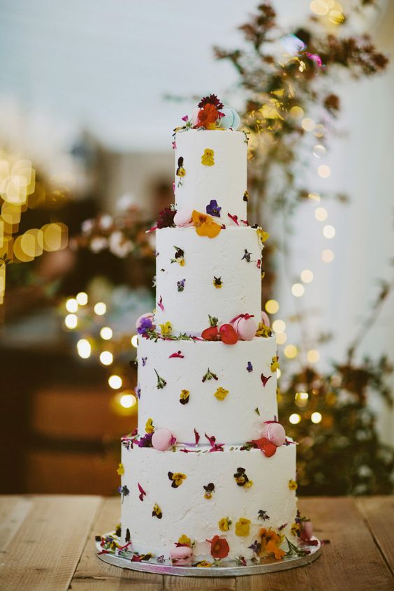 a white buttercream wedding cake with pressed colorful blooms, usual blooms and pink macarons for a bright spring wedding