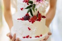a white pattermed wedding cake with figs, red pomegranate sees, a blush flower and greenery for a Valentine wedding