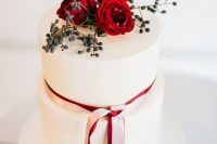 a white wedding cake topped with privet berries, red blooms and a striped blush and red ribbon for a Valentine wedding