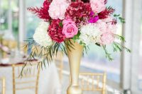 an exquisite Valentine’s Day wedding centerpiece of a gold stand with pink, fuchsia and burgundy blooms and greenery is wow