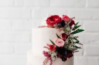 an ombre watercolor pink and red wedding cake topped with beautiful red, pink and purple blooms and greenery