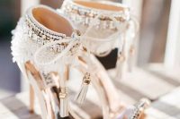 white heavily embellished wedding shoes with thin straps and heavy embellishments on the backs plus tassels