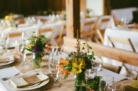 a barn wedding tablescape with a burlap table runner, a colorful floral centerpiece, colorful printed napkins