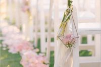 a beautiful and breezy sprign wedding aisle with pink petals on the ground and a cage with pink roses and long tassels is wow