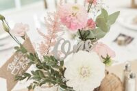 a beautiful barn wedding centerpiece of a wood slice, jars wrapped with lace and twine, pink and white blooms and burlap