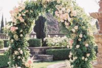 a beautiful circle wedding arch completely covered with greenery and with blush blooms