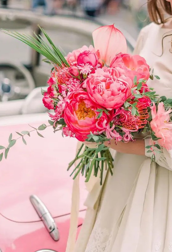 a beautiful pink wedding bouquet of peonies, pincushion peoteas and other flowers and greenery is bold and cool
