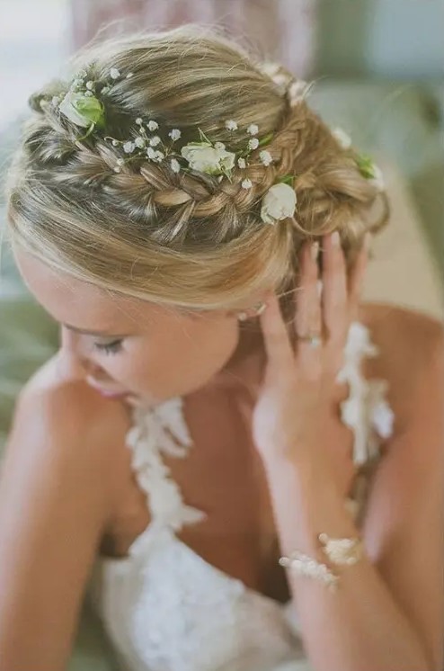 a boho chic braided updo with a curly low bun and some fresh blooms tucked in a beautiful idea for a boho bride