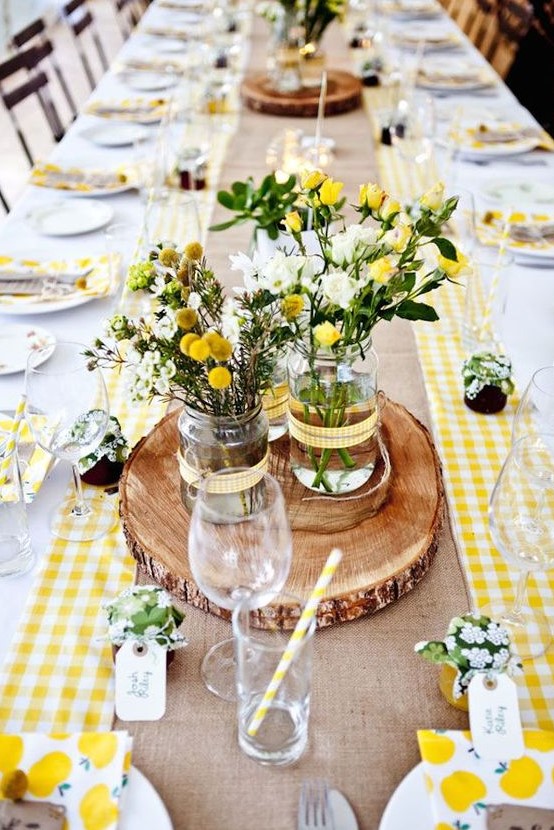 a bright barn wedding table with a burlap runner, bright yellow plaids, a wood slice, printed napkins and jam favors