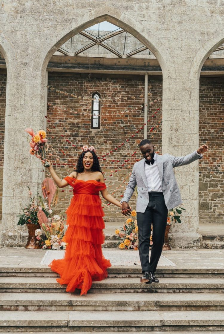 a bright orange off the shoulder ruffle wedding dress with a train and a colorful floral crown