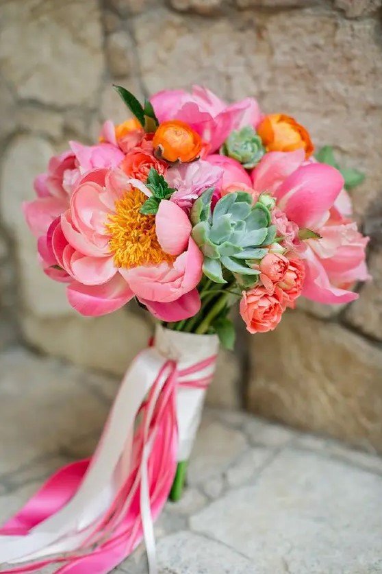 a bright wedding bouquet of pink peonies, orange ranunculus, succulents and pink and neutral ribbon is a lovely solution for summer