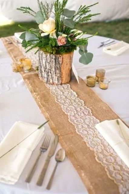 a burlap and lace table runner, a centerpiece of a tree stump with blooms, greenery and evergreens is a lovely idea for a wedding