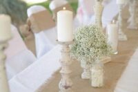 a burlap table runner, wooden candleholders with pillar candles, baby’s breath and smaller candles for a rustic wedding table