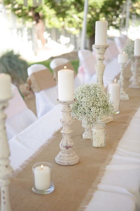 a burlap table runner, wooden candleholders with pillar candles, baby’s breath and smaller candles for a rustic wedding table