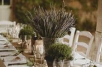 a burlap wedding table runner with some potted greenery as sustainable wedding decor, lavender in a vase and some candles