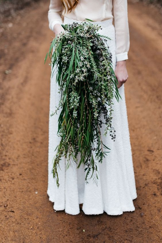 a cascading super long wedding bouquet of various types of foliage and some thistles and blooming branches looks wow