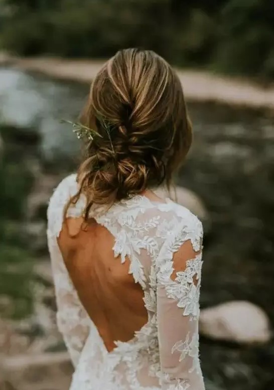 a casual braided and twisted low updo with bangs with some greenery in it is a stylish idea for a casual coastal or beach bride