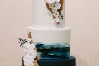 a catchy wedding cake with a white tier, a brushstroke one and a plain one, with white sugar blooms, gold touches and berries