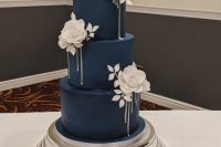 a chic navy wedding cake with large white roses and leaves looks breathtakingly elegant