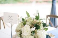 a chic table setting with a white hydrangea wedding centerpiece, candles and a navy table runner