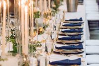 a chic tablescape with a white tablecloth, navy napkins, greenery garlands and candles is very stylish