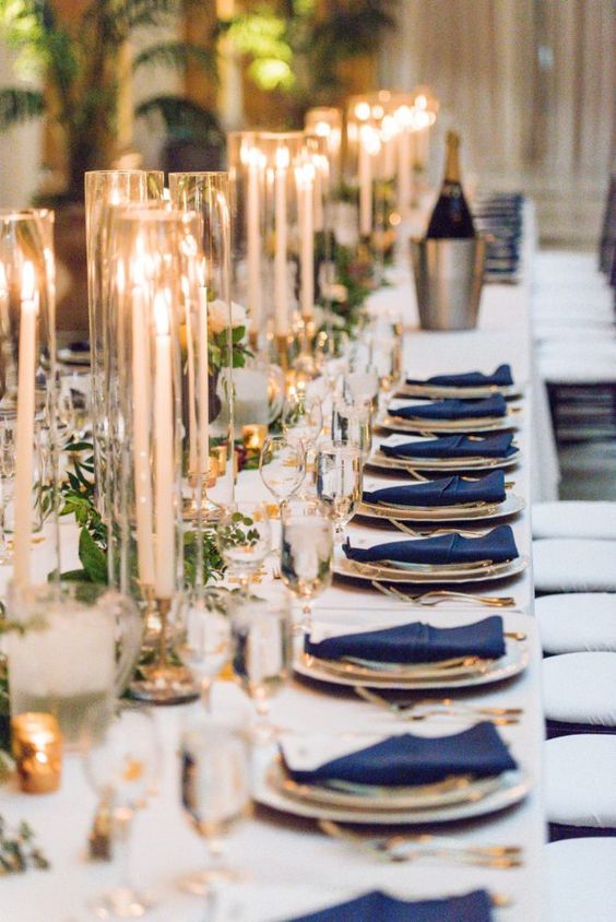 a chic tablescape with a white tablecloth, navy napkins, greenery garlands and candles is very stylish