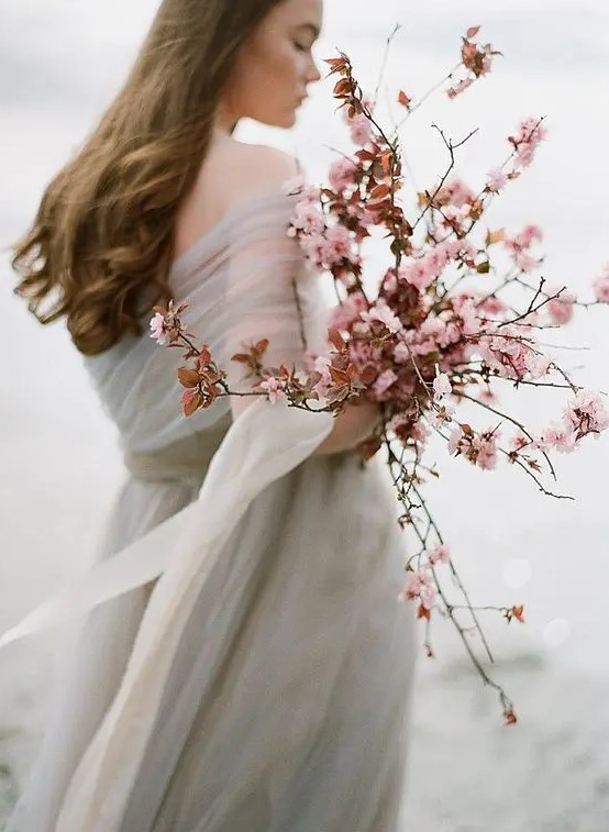 a coastal bride rocking a pink cherry blossom wedding bouquet that contrasts her grey wedding dress