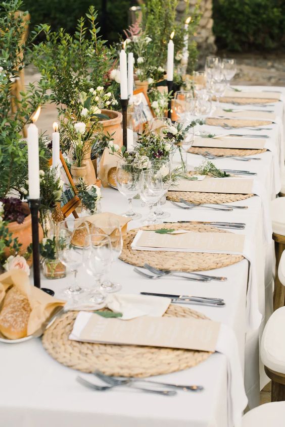 a cozy rustic wedding tablescape with potted greenery and blooms, tall candles, woven placemats and family pics is amazing