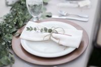 a delicate backyard wedding table setting with neutral linens, a porcelain charger and white plates, a eucalyptus runner