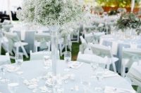 a delicate backyard wedding tablescape with a blue tablecloth, white napkins and a tall baby’s breath centerpiece plus petals on the table