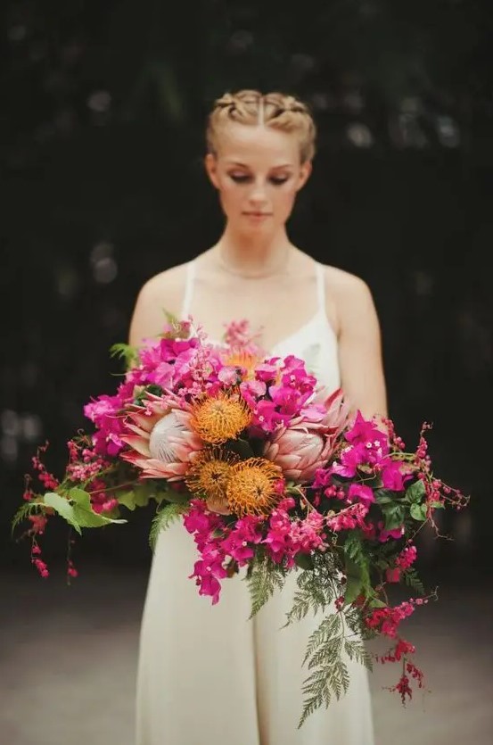 a dimensional and textural cascading wedding bouquet of hot pink blooms, pincushion proteas, king proteas, greenery and leaves for a bold wedding