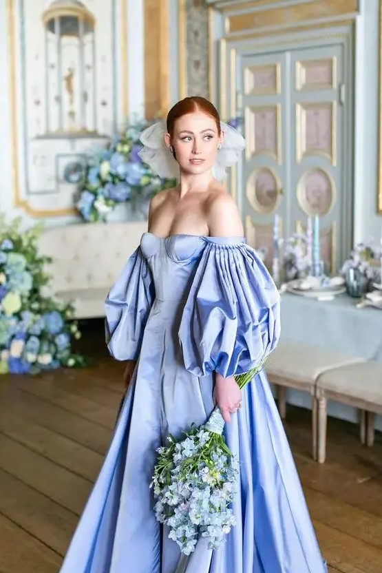 a fantastic royalty inspired off the shoulder blue wedding dress with a corset, puff sleeves and a pleated skirt plus a veil bow