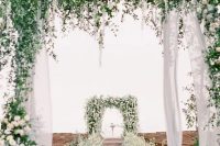 a fantastic wedding ceremony space with arches decorated with white and blue blooms and greenery, with maching arrangements lining up the aisle