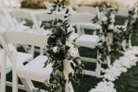 a fresh and edgy spring wedding aisle with white petals on the ground, with white blooms and greenery arrangements on the chairs