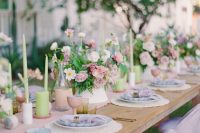a fun pastel backyard wedding tablescape with a pink runner, pink blooms and goblets, green candles and greenery plus lilac napkins