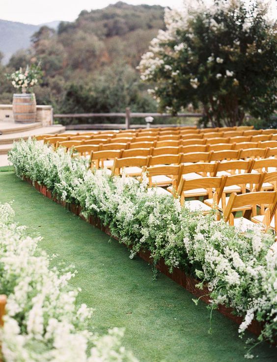 a gorgeous rustic wedding aisle with super lush greenery and white florals in planters is a fantastic idea to support that flourishing feel of spring