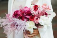 a jaw-dropping pink wedding bouquet of fuchsia, red and blush and white blooms and light pink dried leaves, blush ribbon
