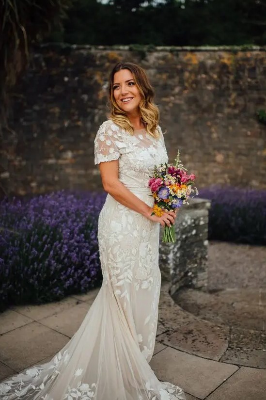 a lace applique mermaid wedding dress with short sleeves, a high neckline and a long train