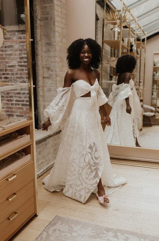 a lace two piece wedding dress wiht a crop top with long sleeves and a pleated maxi skirt with a train for a boho bride